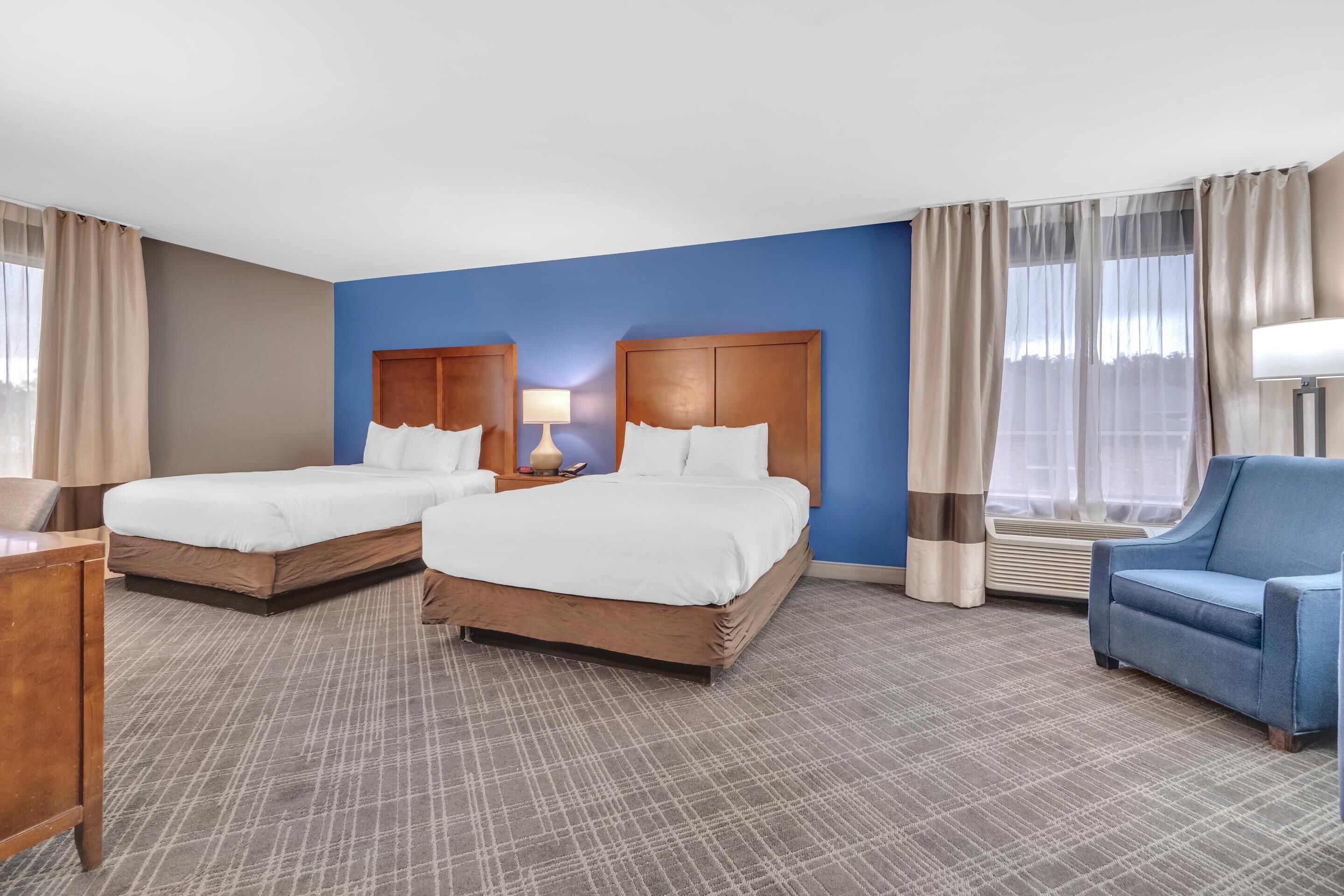 Habitación de hotel con dos camas, un escritorio, una silla y una ventana con cortinas.