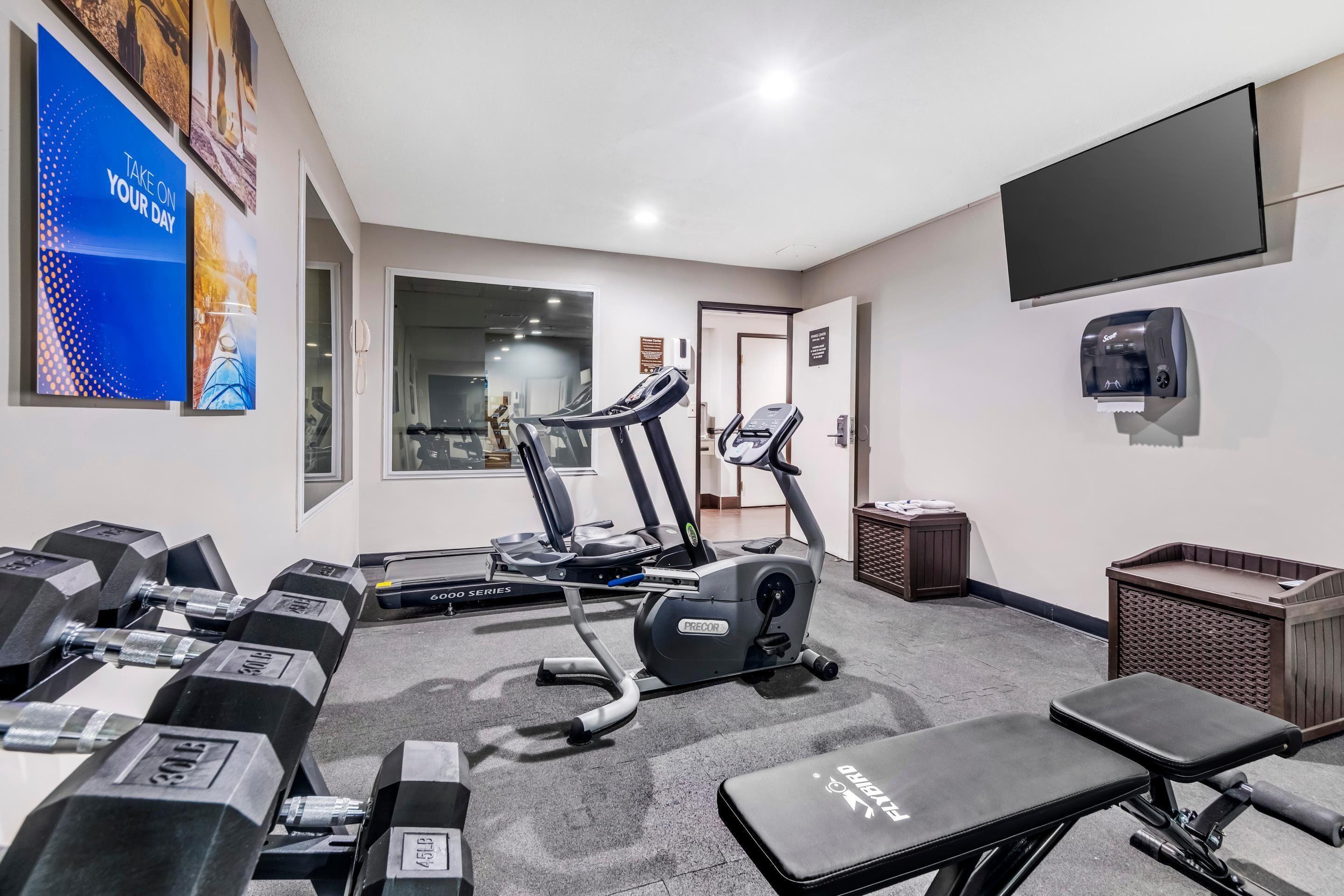 Ein Fitnessstudio mit Laufbändern, Kurzhanteln und einer Bank.