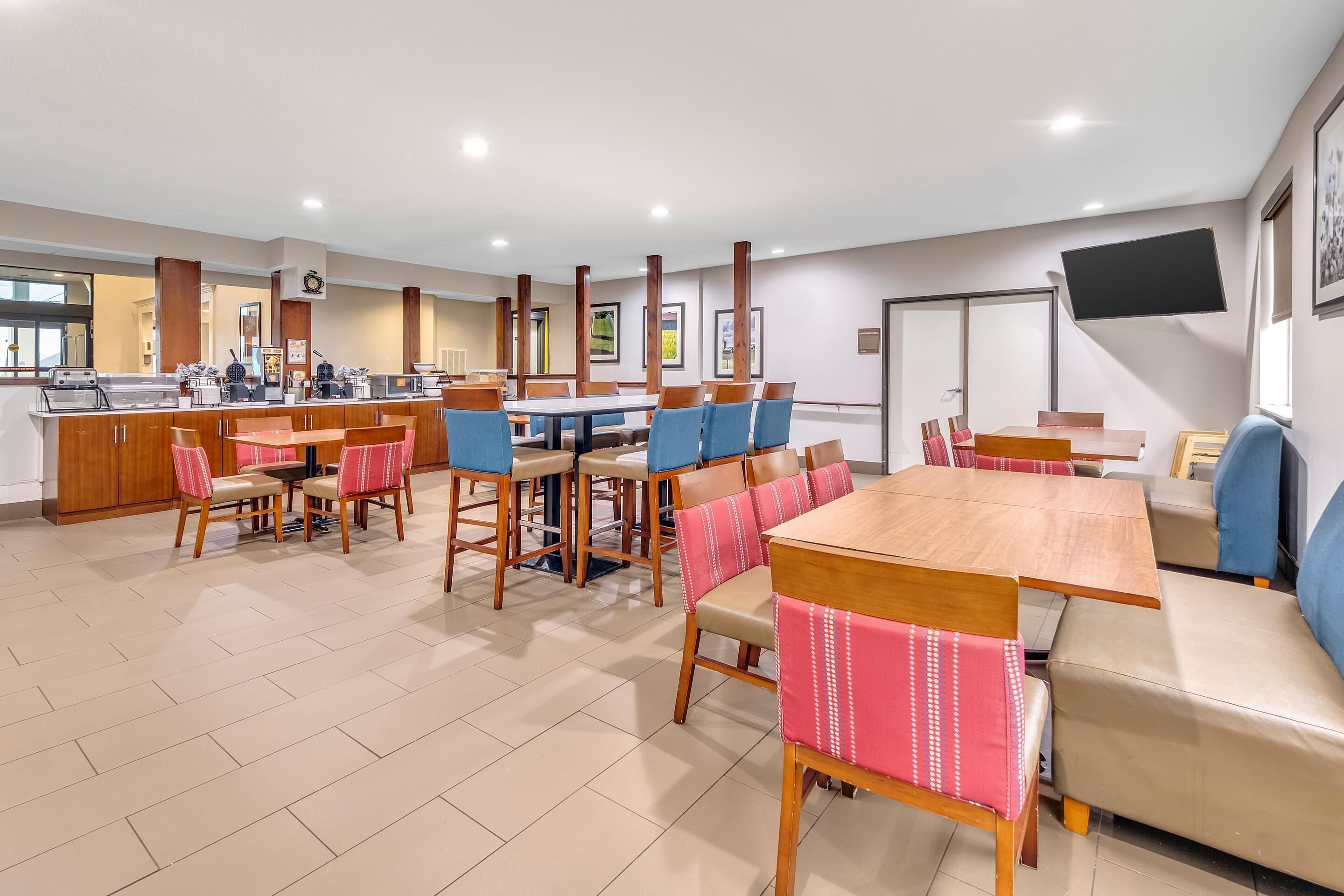Un espace de restauration d’hôtel comprenant plusieurs tables et chaises, un comptoir avec des machines à café et un téléviseur fixé au mur.