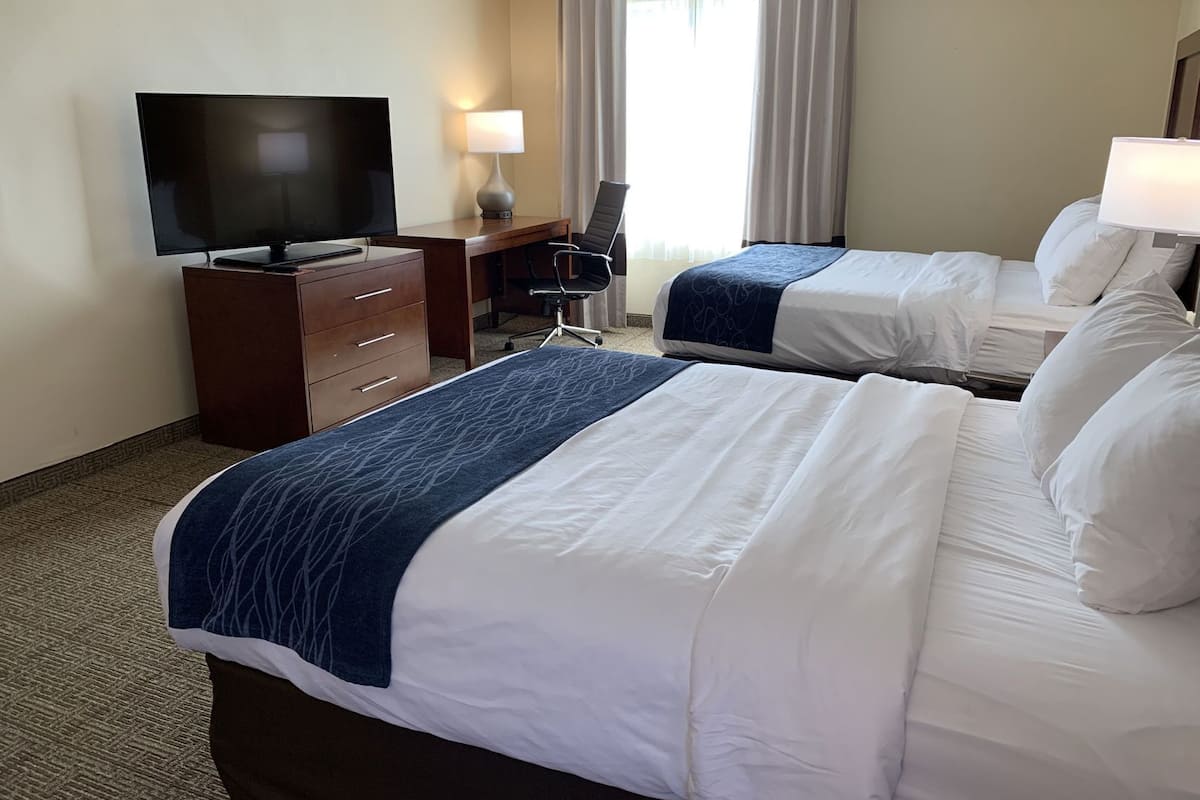 A hotel room with two beds, a desk with a TV, a chair, and a lamp.