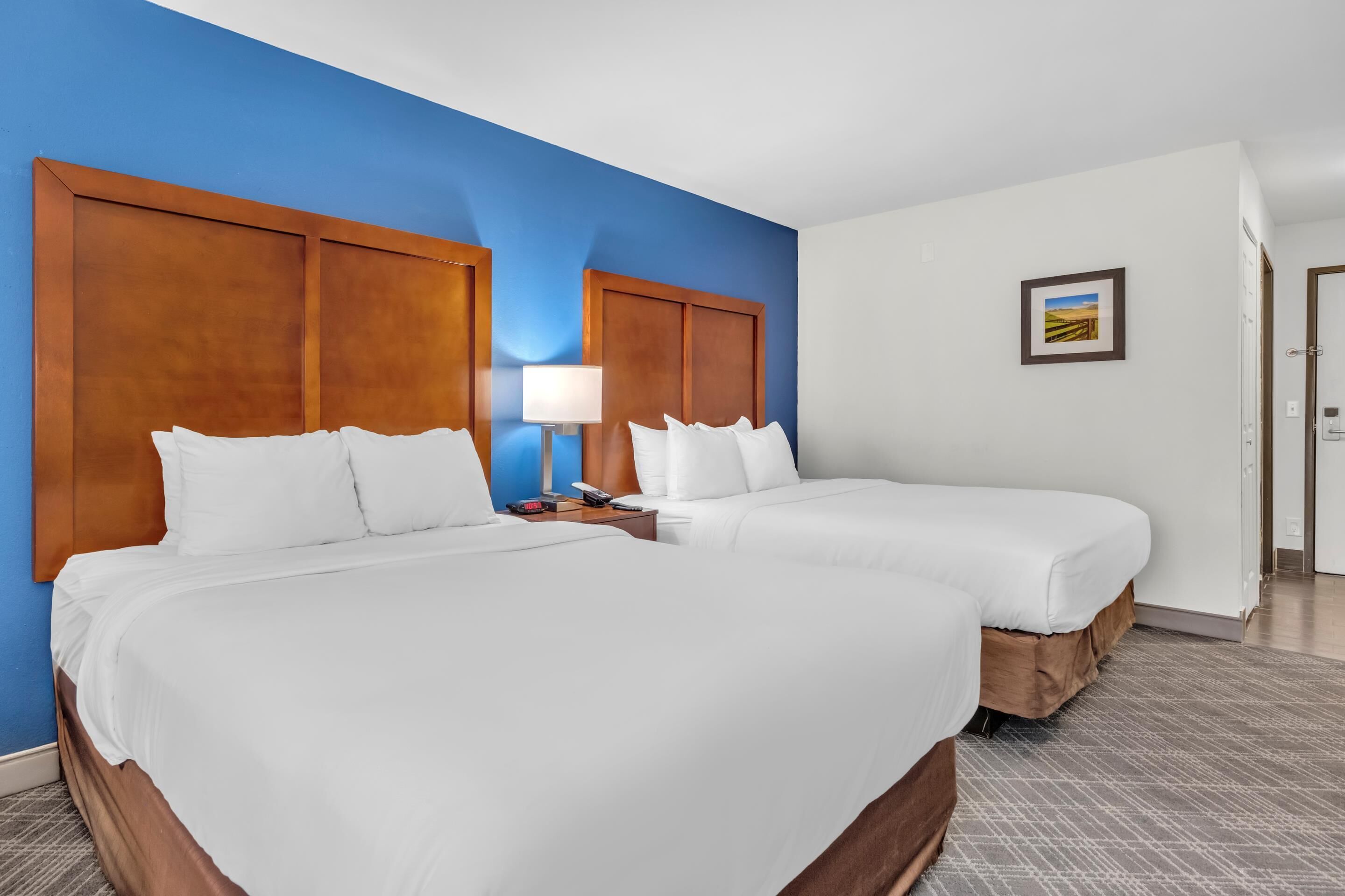 A hotel room with two beds, a nightstand with a lamp, and a framed picture on the wall.