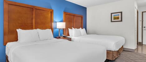 A hotel room with two beds, a nightstand with a lamp, and a framed picture on the wall.
