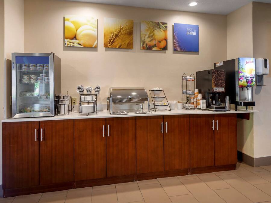 A breakfast bar with a refrigerator, coffee machine, juice dispenser, and various food items.