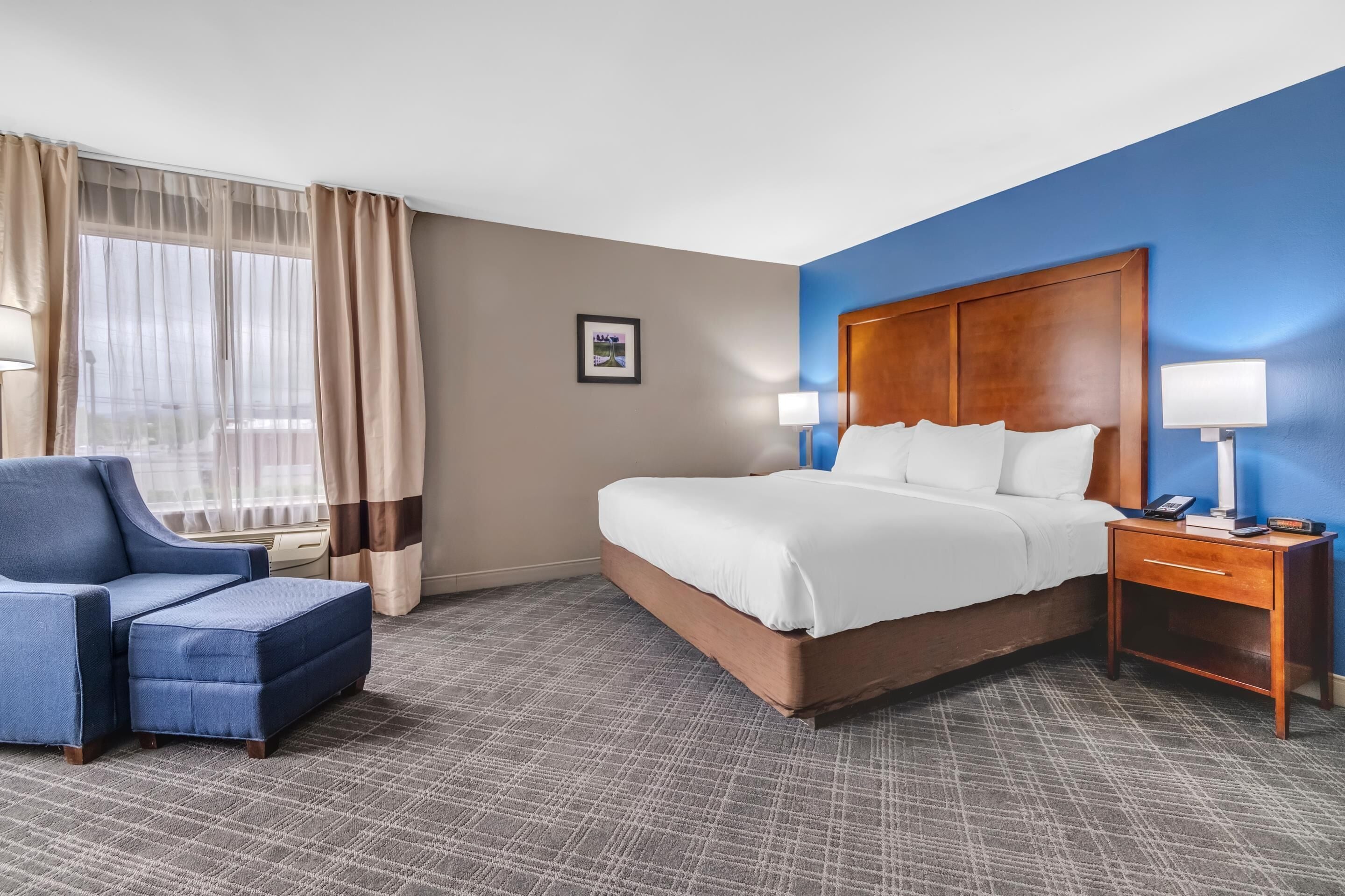 Una habitación de hotel con cama, una silla, una mesita de noche y una ventana con cortinas.