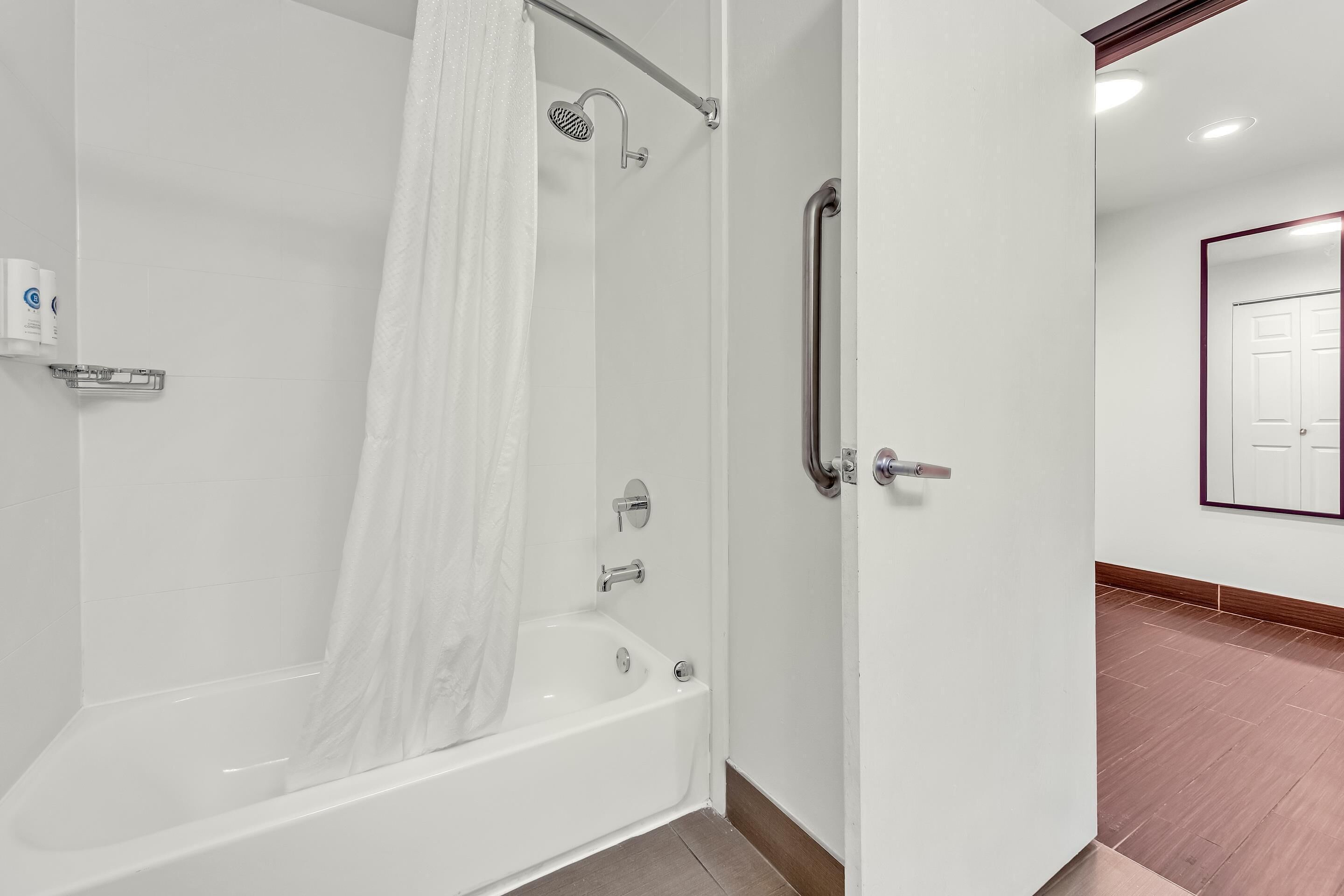 Une salle de bain moderne dotée d’une douche à l’italienne, d’une baignoire entourée de parois en verre et d’une porte avec une poignée.