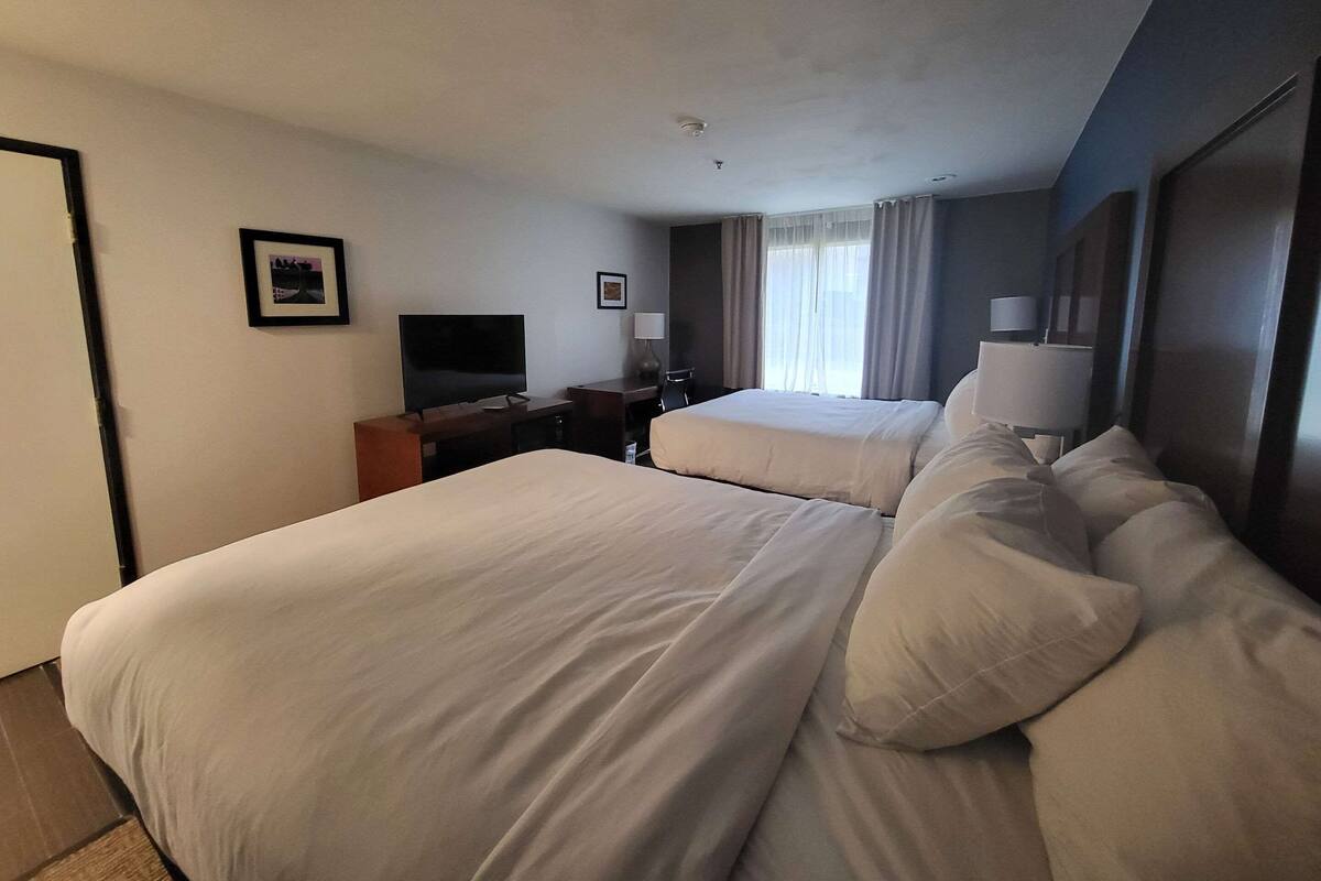 A hotel room with two beds, a desk, a television, and a window with curtains.