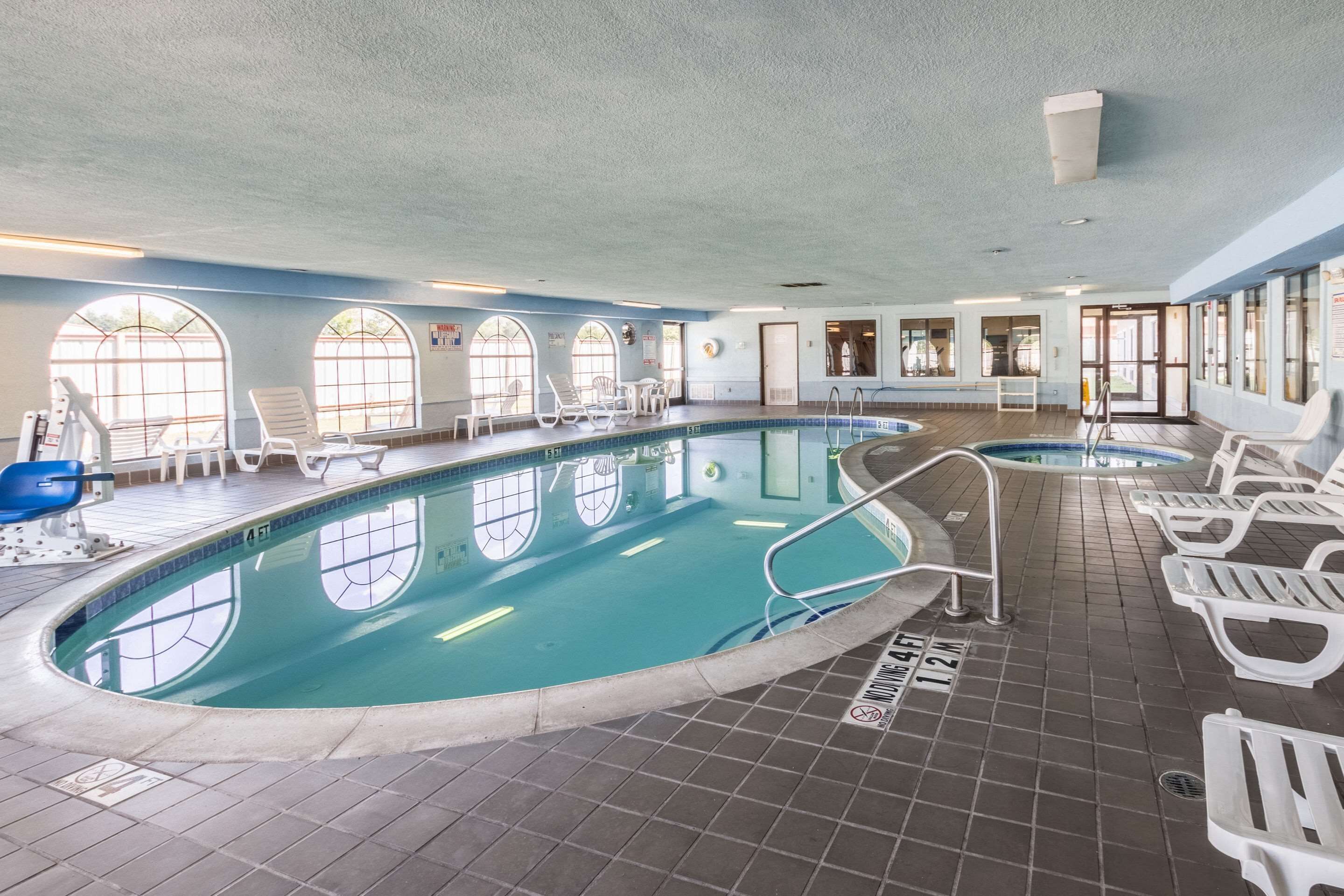 En indendørs swimmingpool med krystalklart vand, flisebelagt gulv og flere liggestole hele vejen rundt.