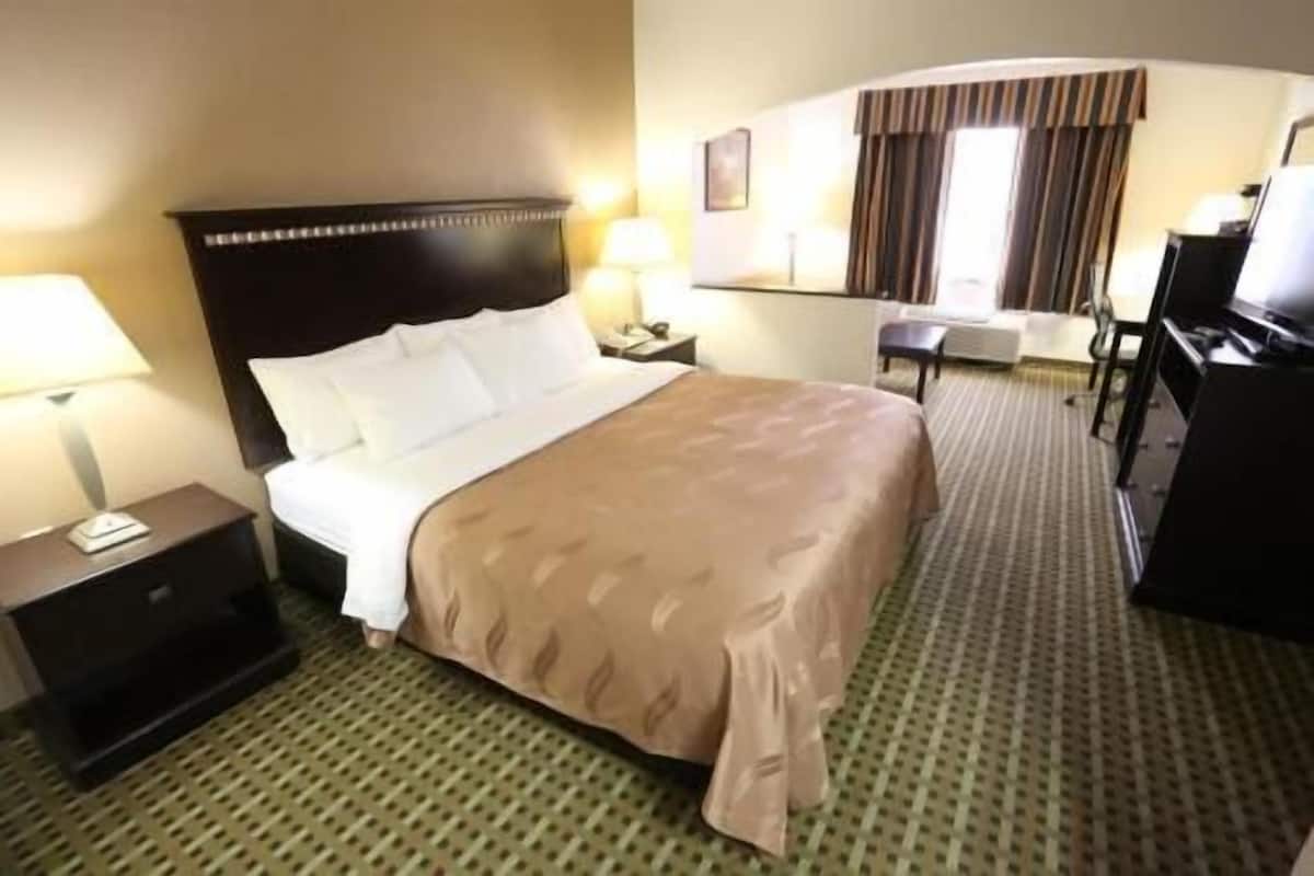 Ein Hotelzimmer mit einem Bett, einem Schreibtisch, einem Stuhl, einer Lampe und einem Fernseher.