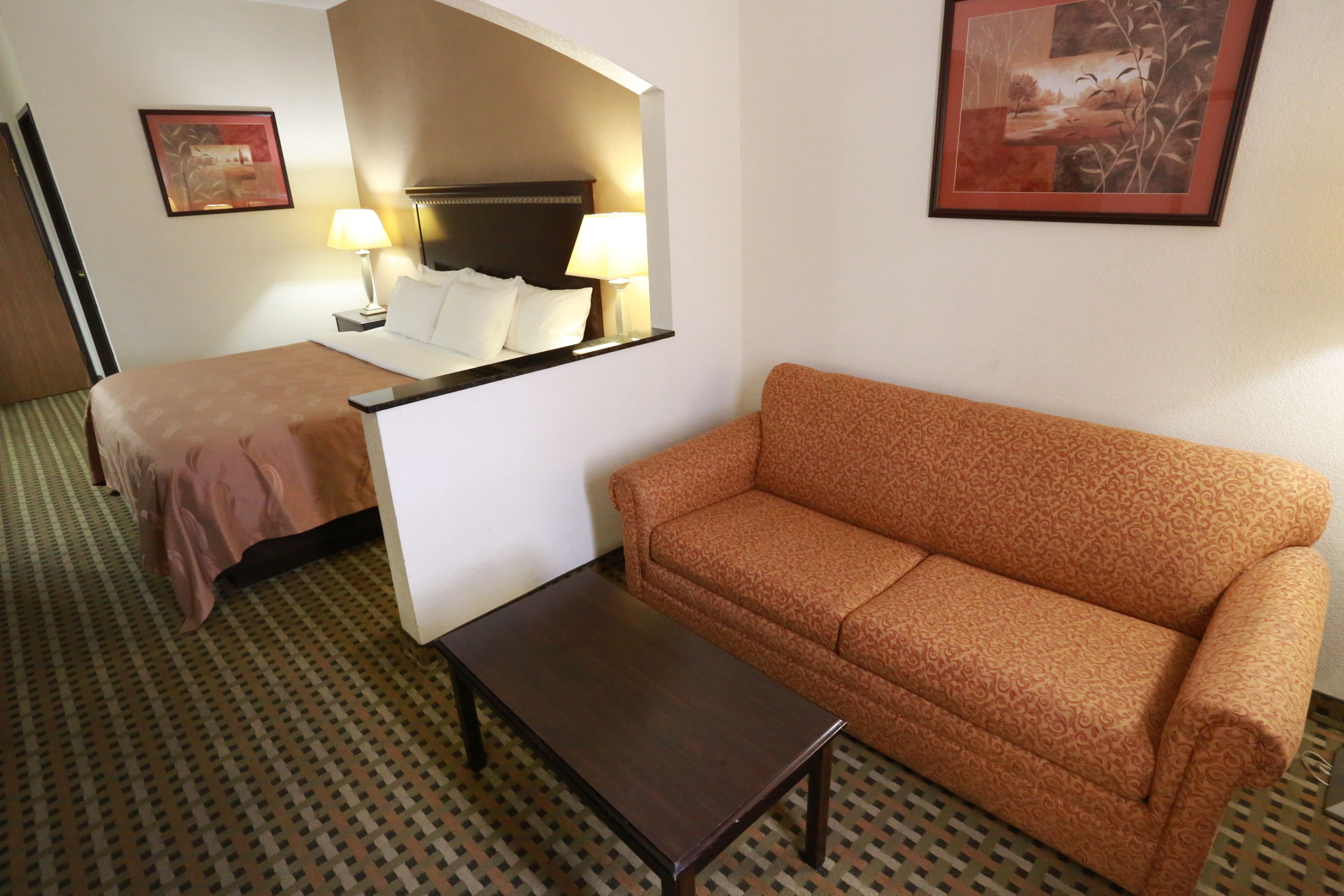 Una habitación de hotel con cama, sofá, una mesita y dos lámparas.