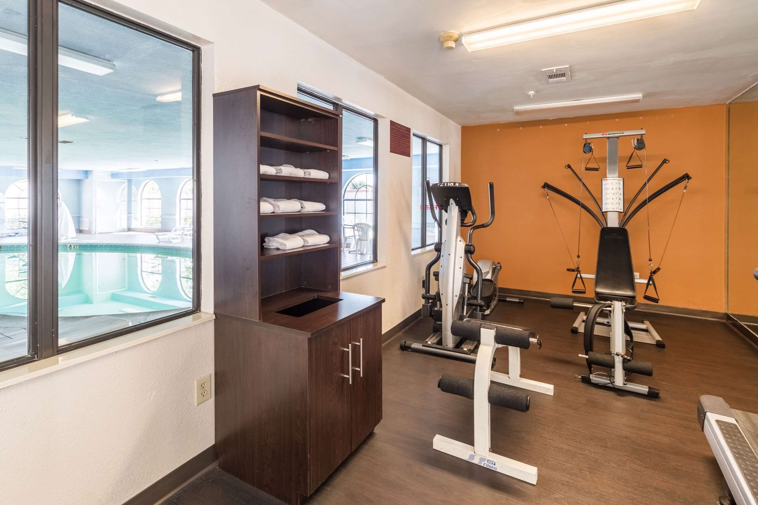 Un gimnasio con equipo de ejercicio, un armario de madera con toallas y ventanas amplias.