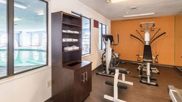 Un gimnasio con equipo de ejercicio, un armario de madera con toallas y ventanas amplias.