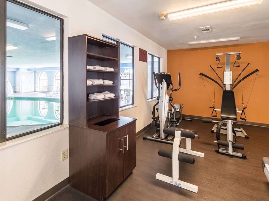 Un gimnasio con equipo de ejercicio, un armario de madera con toallas y ventanas amplias.