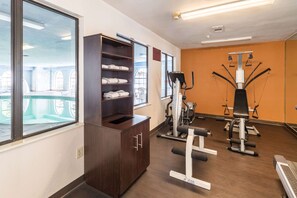 A gym with exercise equipment, a wooden cabinet with towels, and large windows. - Quality Suites Burleson - Ft. Worth (Burleson)