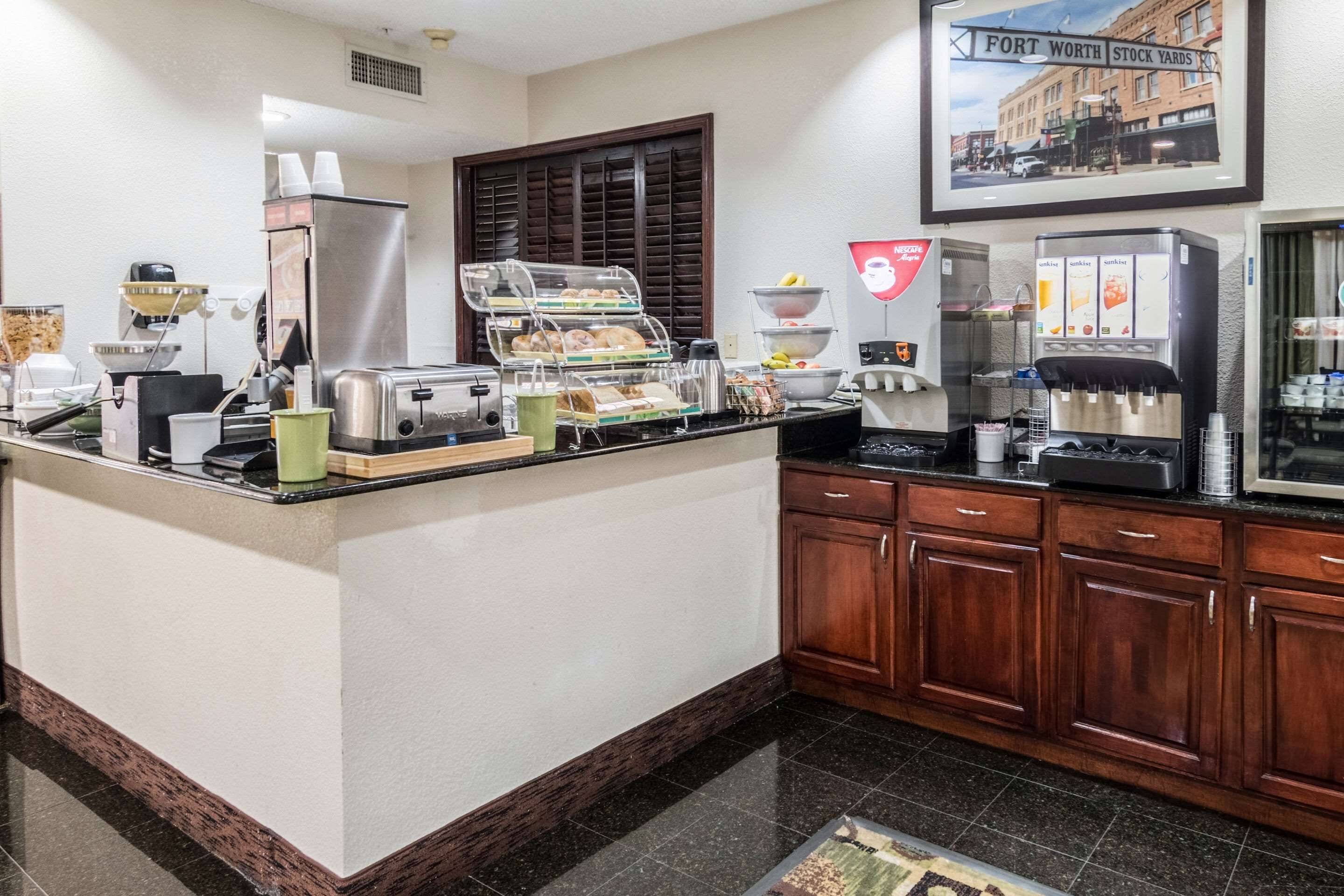 A hotel kitchen with a buffet counter, coffee machines, and a framed picture of Fort Worth Stock Yards.