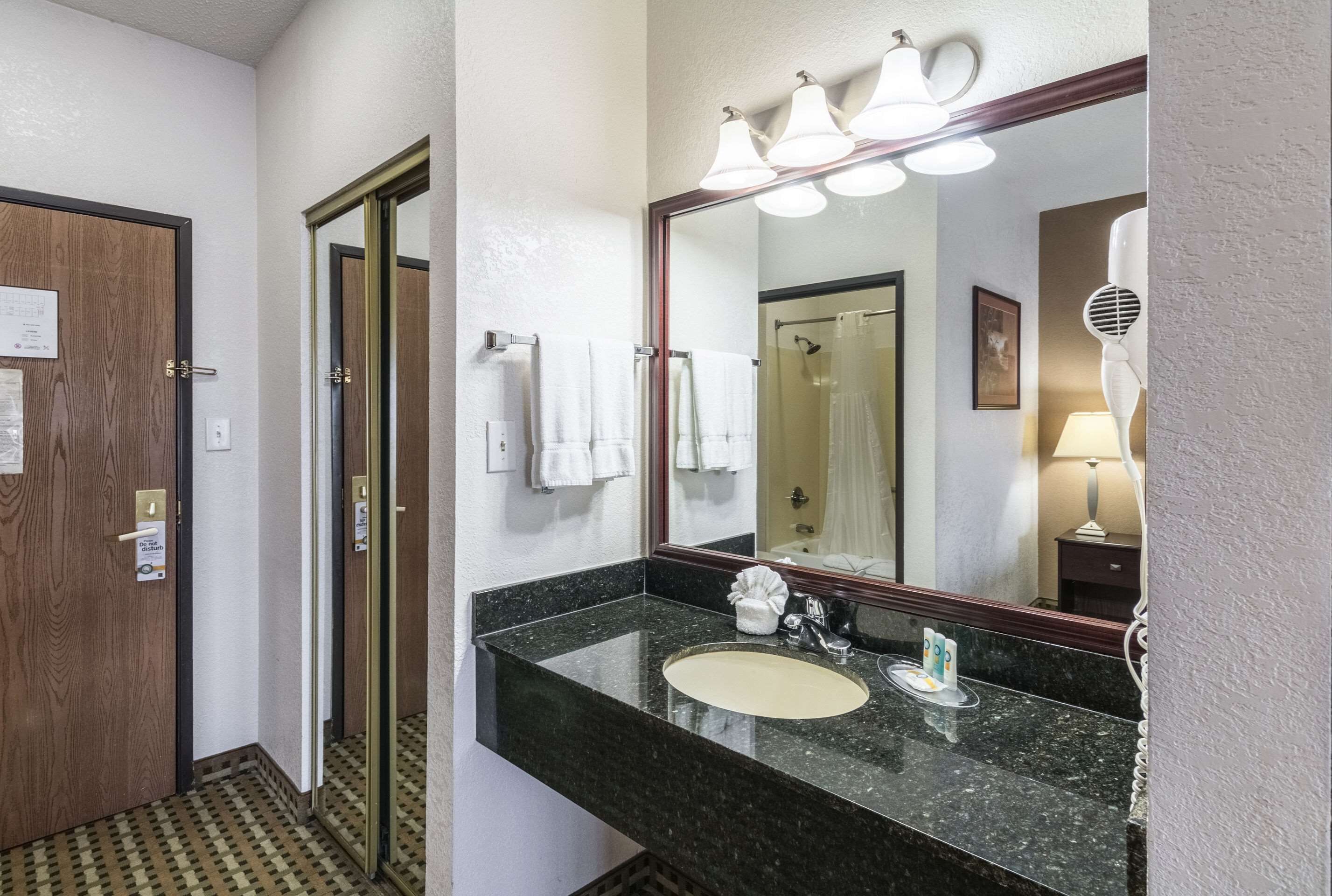 A hotel bathroom with a granite countertop sink, a large mirror, and a towel rack.