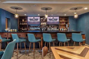 A bar area with a counter, bar stools, and shelves stocked with bottles and glasses. - Four Points by Sheraton Anchorage Downtown (Anchorage)