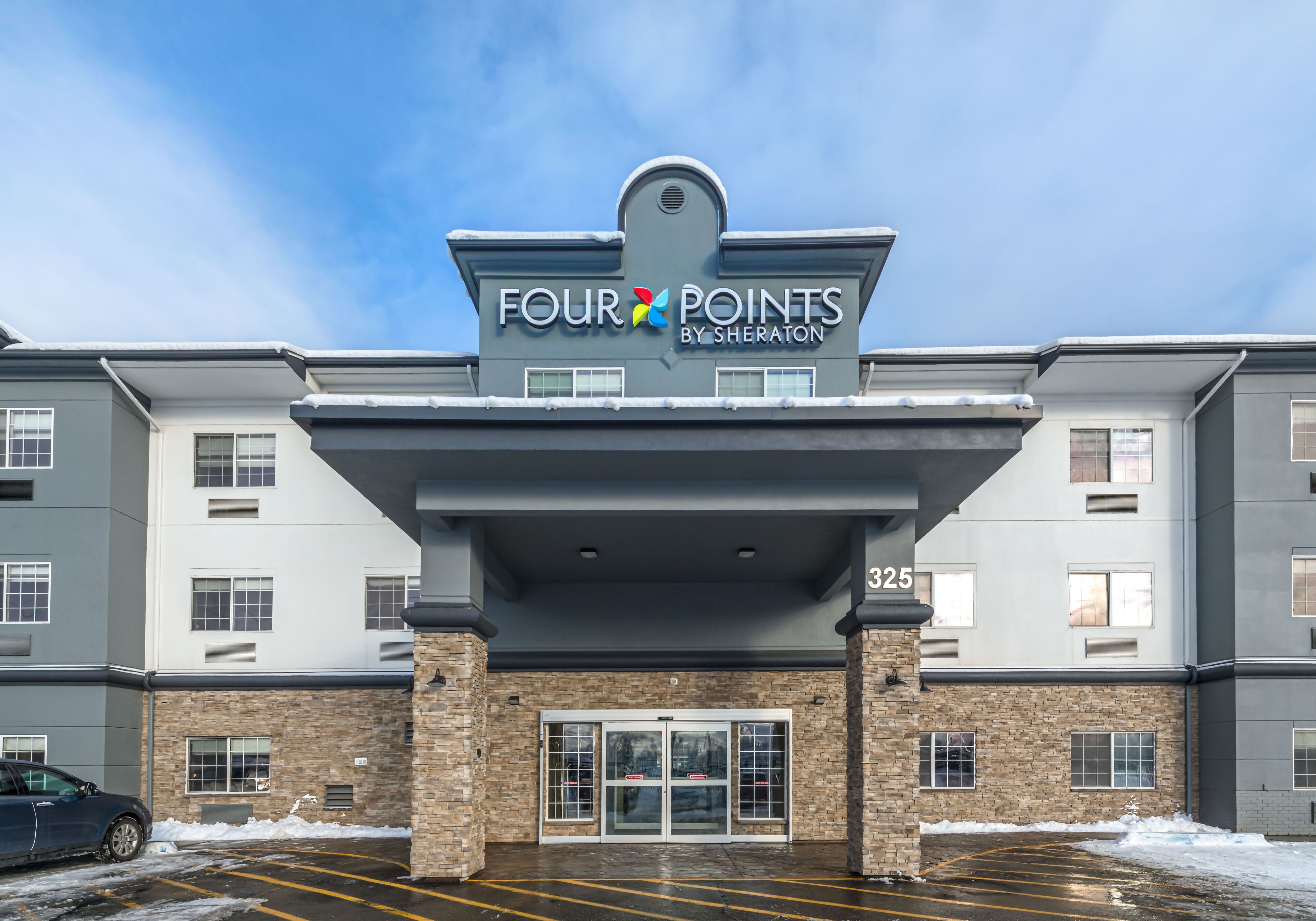 En hotellentrén till ett Four Points by Sheraton-hotell med en fasad av tegel, dubbeldörrar och en parkeringsplats.