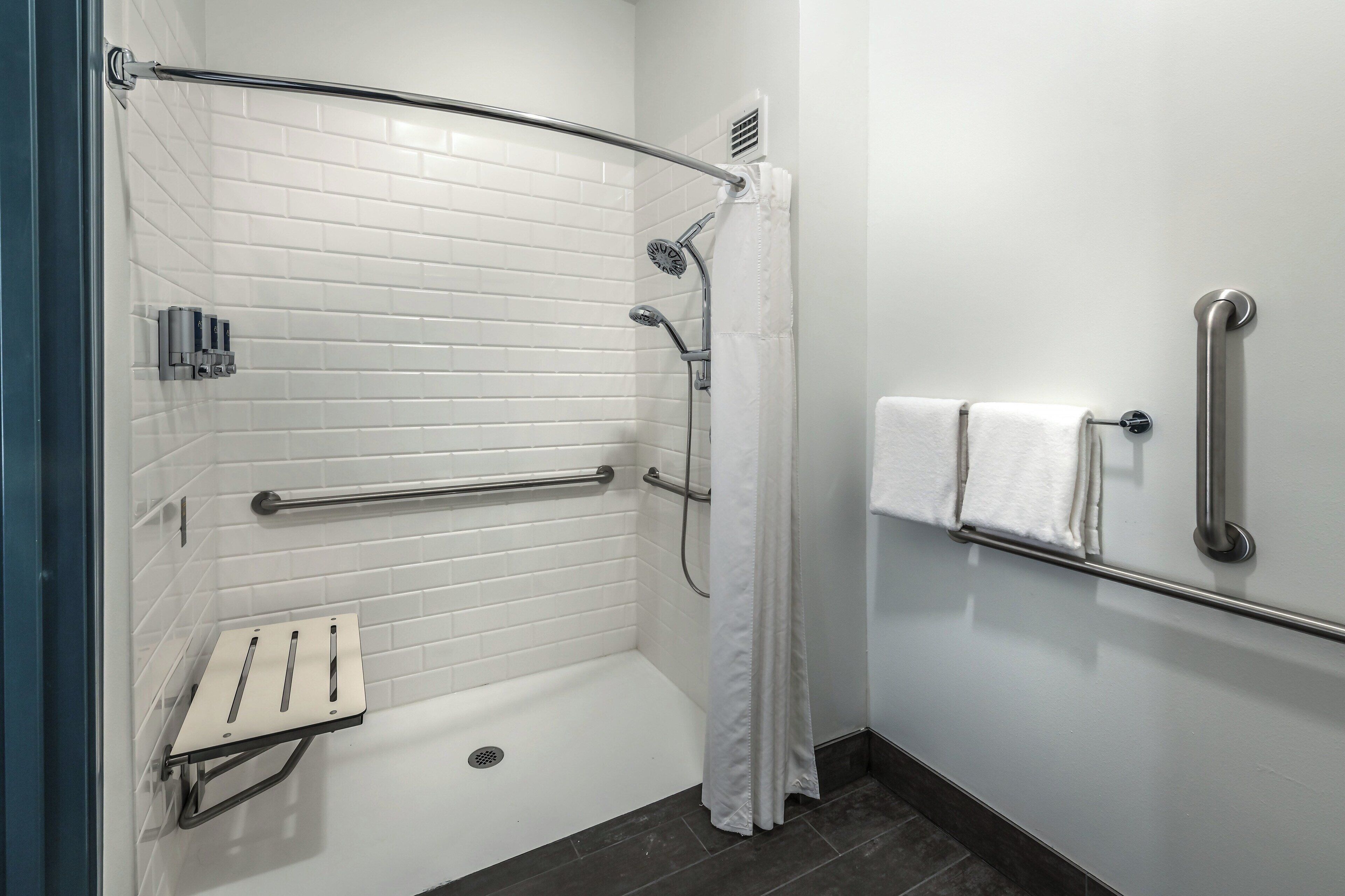 A modern bathroom with white tiled walls, a shower with a glass door, and a grab bar for safety.