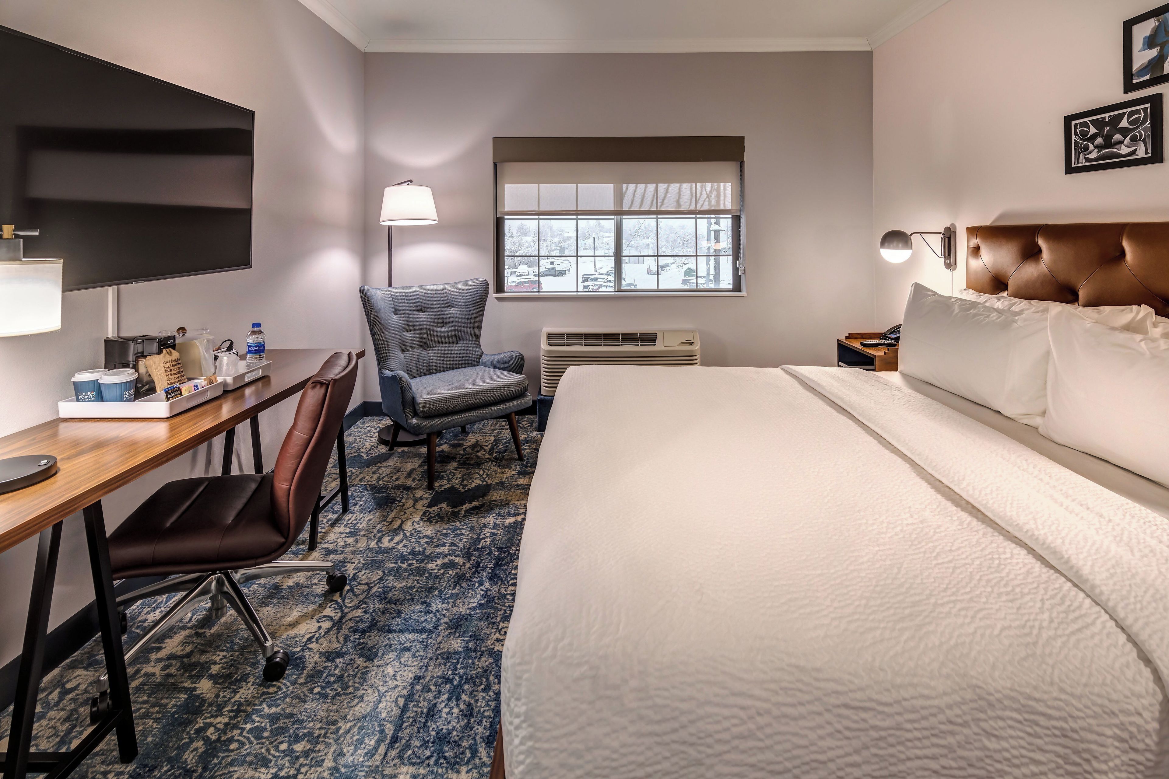 Habitación de hotel con cama, escritorio, silla y ventana con vista al exterior.
