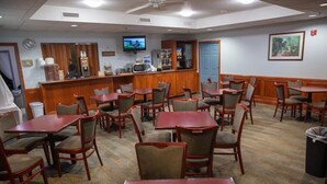 Une chambre d’hôtel dotée d’un coin repas avec des tables et des chaises en bois, d’un bar avec un téléviseur et d’un tableau accroché au mur.