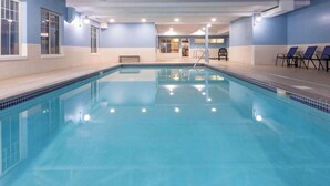 Une piscine intérieure à l’eau claire, entourée de murs percés de fenêtres et agrémentée d’un banc.