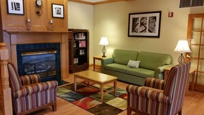 A cozy living room with a fireplace, striped armchairs, a green sofa, and a bookshelf. - Country Inn & Suites by Radisson, Bloomington-Normal West, IL (Bloomington)