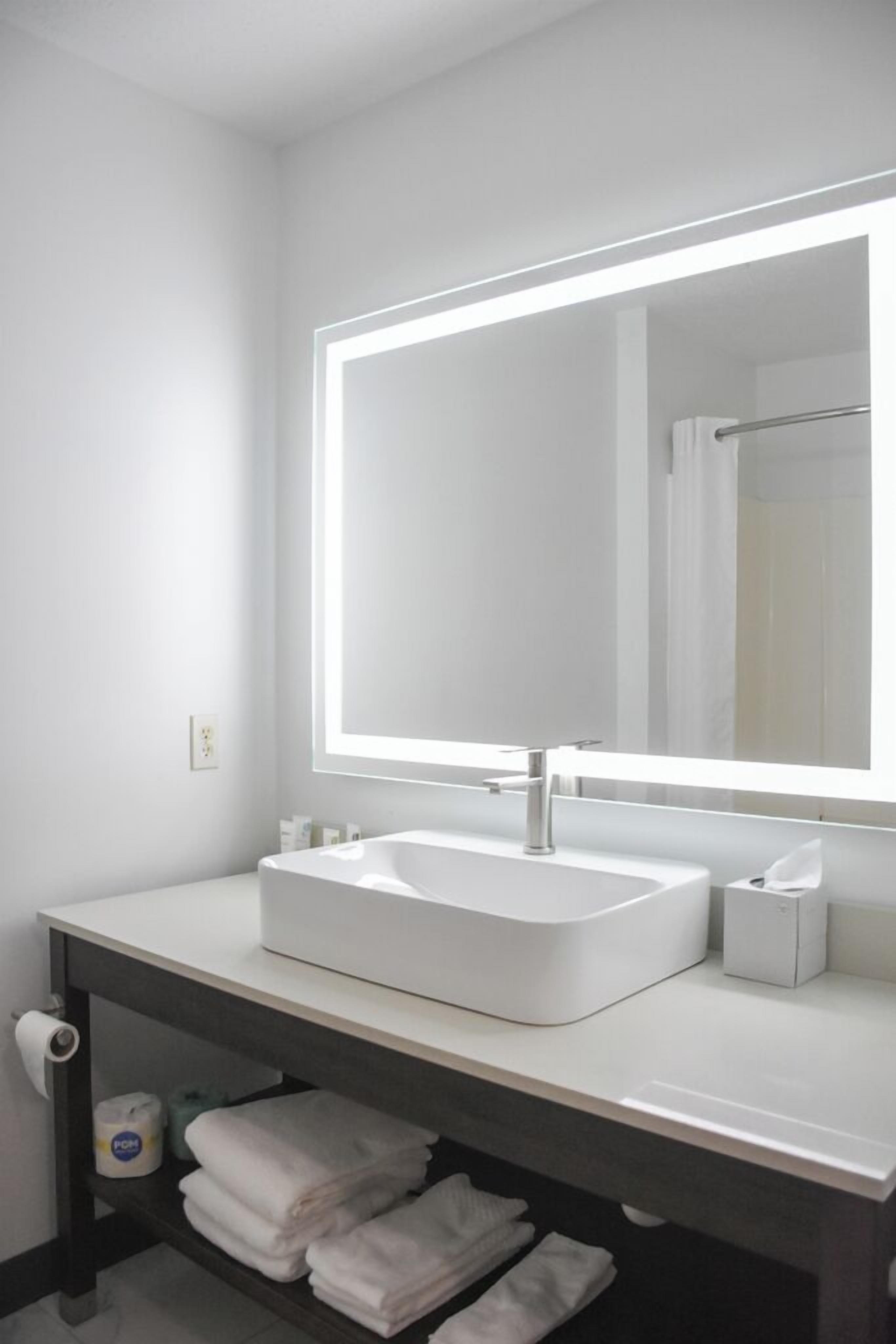 A modern bathroom with a white sink, a large mirror, and a towel rack.