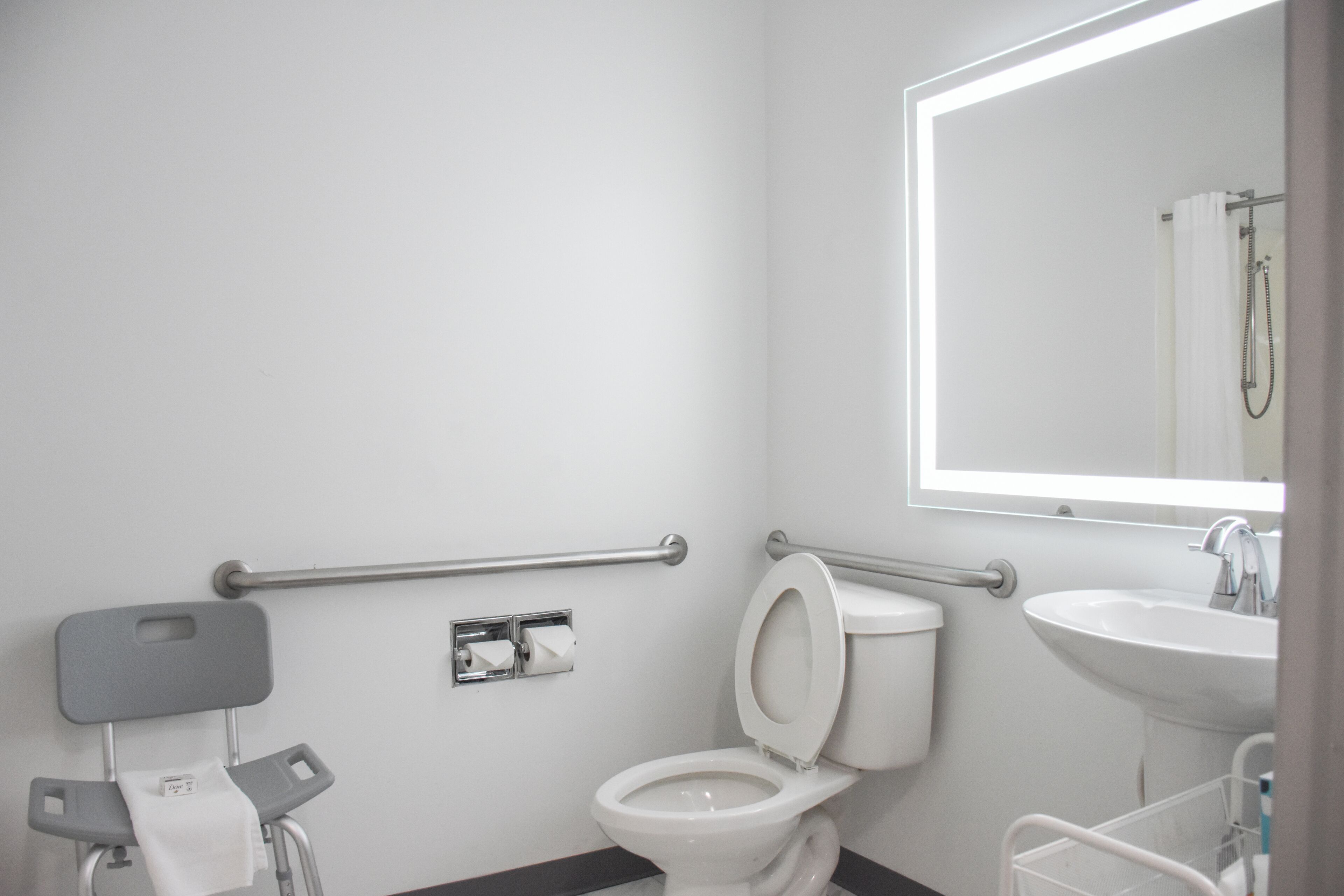A modern bathroom with a white toilet, a sink, a mirror, and a grab bar.