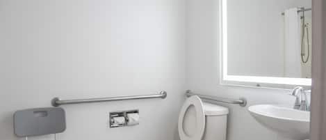 A modern bathroom with a white toilet, a sink, a mirror, and a grab bar.