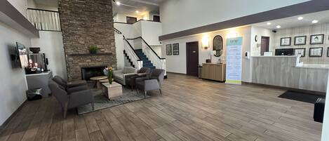 A spacious lobby with a stone fireplace, a staircase, and a reception desk.