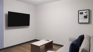 A modern living room with a flat-screen TV mounted on the wall, a wooden coffee table, and a grey sofa with blue cushions.