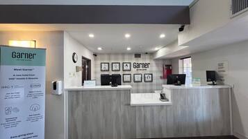 A hotel reception area with a modern design, featuring a reception desk, framed artwork on the wall, and a signboard promoting hotel rewards.