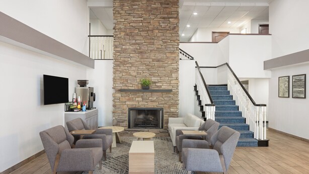 A spacious living area with a stone fireplace, comfortable seating, a flat-screen TV, and a staircase. - Garner Hotel Phoenix Northwest – Surprise by IHG (Surprise)
