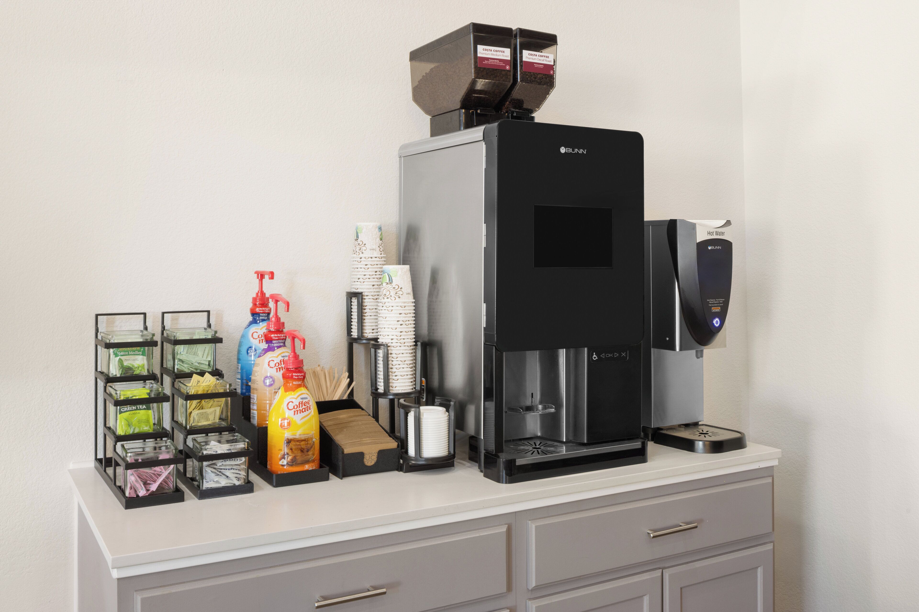 En kaffemaskine med kaffedispenser, en varmtvandsdispenser og en kaffekværn på en bordplade.