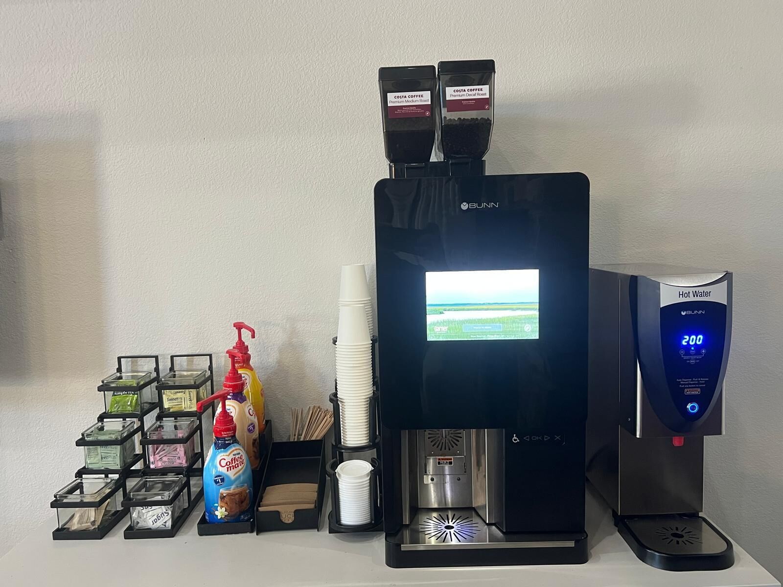 A coffee station with a coffee machine, a hot water dispenser, and various coffee pods and syrups.