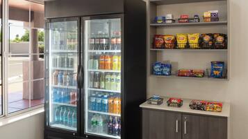 A vending machine stocked with beverages and snacks, including Lay's and Doritos, in a room with a window and a cabinet.