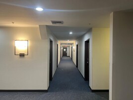 Un pasillo largo y estrecho en un hotel, con suelo alfombrado, puertas a ambos lados e iluminación empotrada en el techo.
