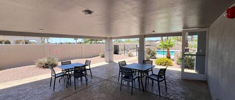 A covered patio area with a pool view, featuring a table and chairs arrangement.