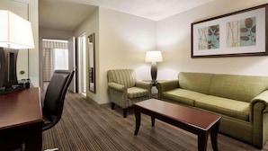 A hotel room with a wooden desk, a green sofa, a striped armchair, a lamp, and a framed picture on the wall.
