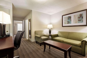 A hotel room with a wooden desk, a green sofa, a striped armchair, a lamp, and a framed picture on the wall. - Country Inn Suites By Radisson Kingsland Ga (Kingsland)