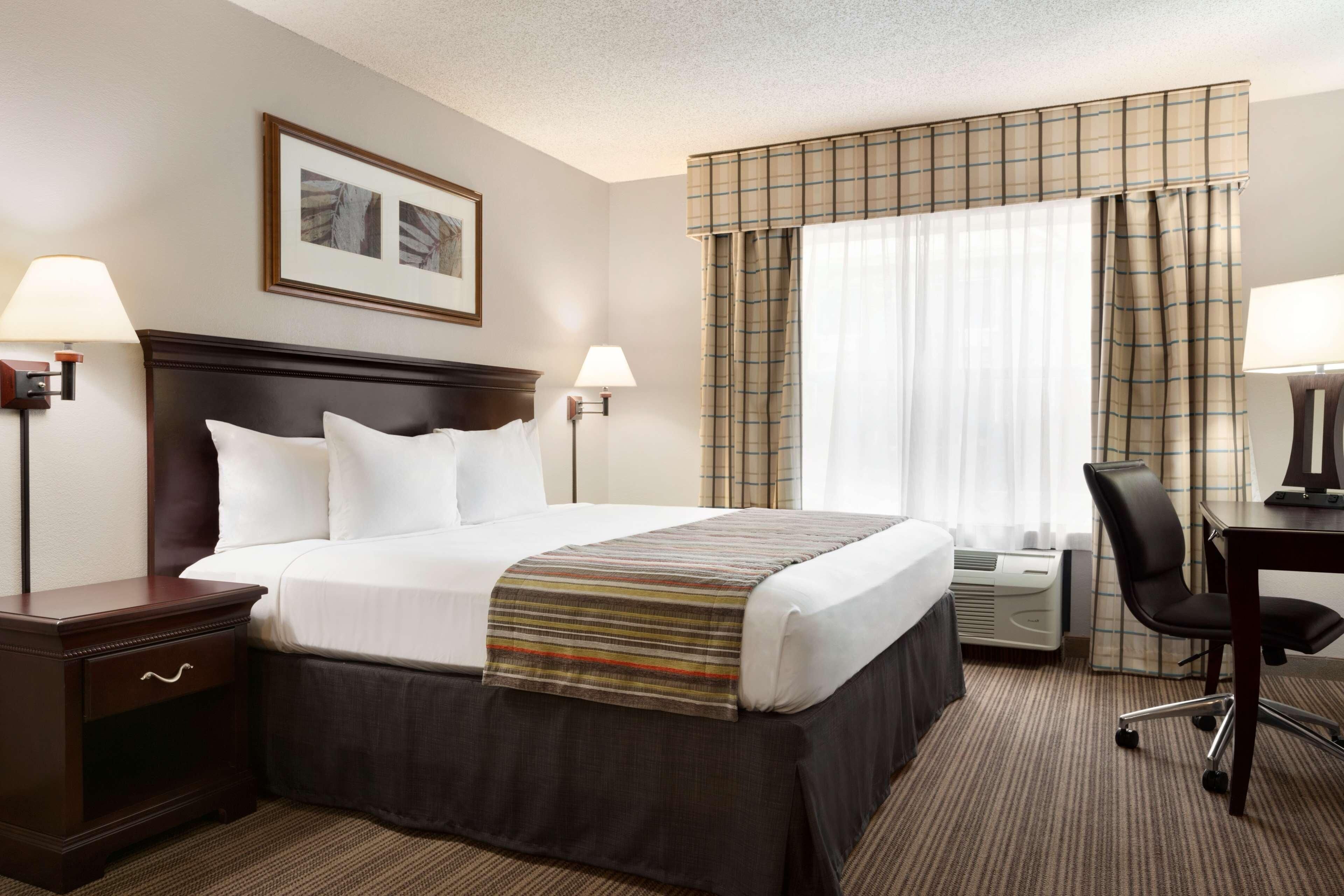 A hotel room with a large bed, two bedside lamps, a desk with a chair, and a window with curtains.