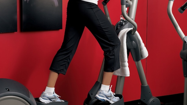 A woman using a stationary bike in a gym with red walls and multiple exercise machines.