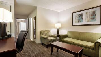 Quarto de hotel com escrivaninha, poltrona listrada, sofá verde, luminária e quadro na parede.