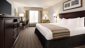 A hotel room with a large bed, a desk with a chair, a television, and two lamps.