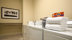 A laundry area with a stacked white towel, a Tide detergent box, and a framed picture on the wall.