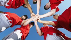 En grupp människor i röda och vita sportkläder som bildar en cirkel genom att hålla händerna samman.