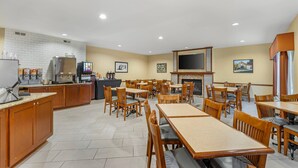 A spacious dining area with wooden tables and chairs, a kitchen area with a refrigerator and coffee machines, and a fireplace.
