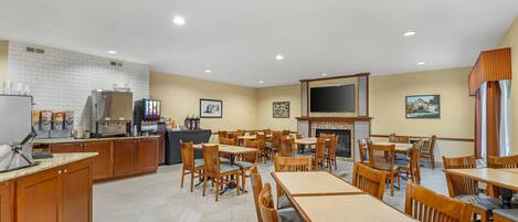 A spacious dining area with wooden tables and chairs, a kitchen area with a refrigerator and coffee machines, and a fireplace.