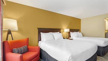 A hotel room with two beds, a red armchair, and a lamp.