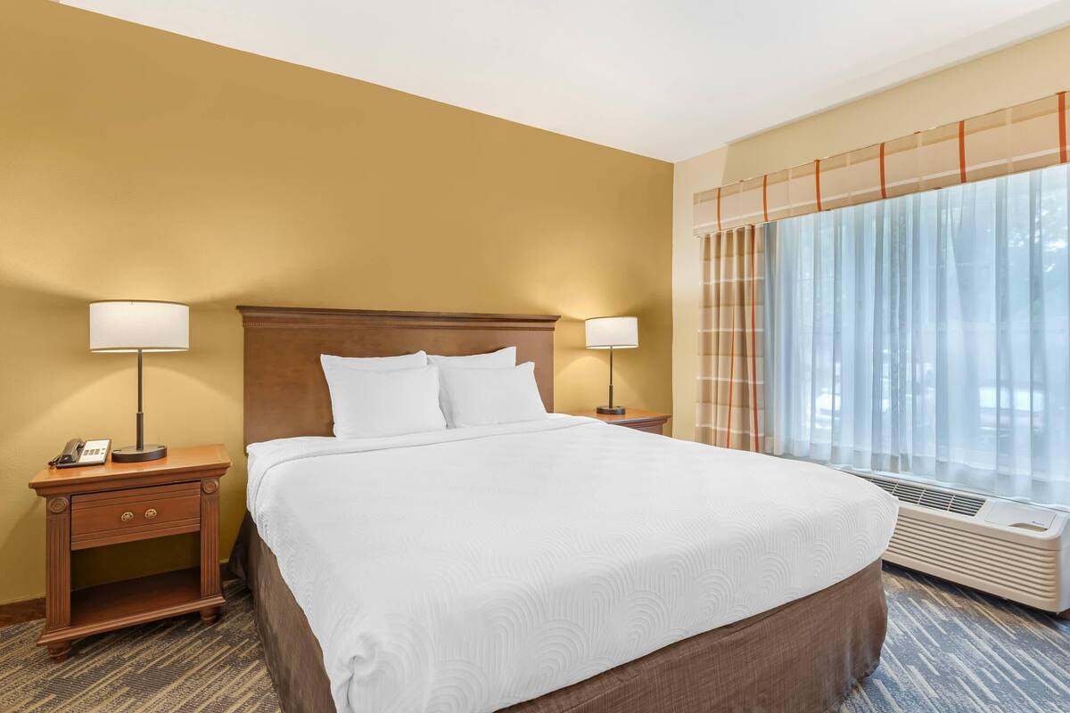 A hotel room with a large bed, two bedside tables with lamps, a telephone, and a window with curtains.